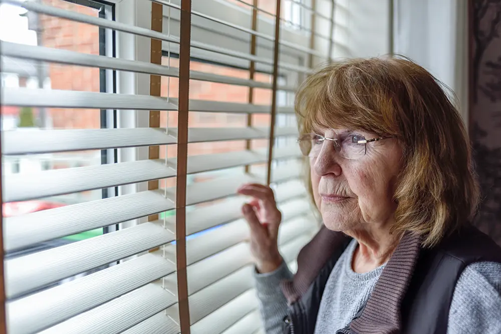 Older woman is looking out a window in deep thought